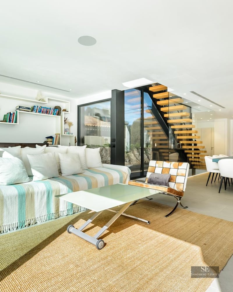 Bright modern living room with a striped sofa, floating wooden stairs, and a black freestanding fireplace.