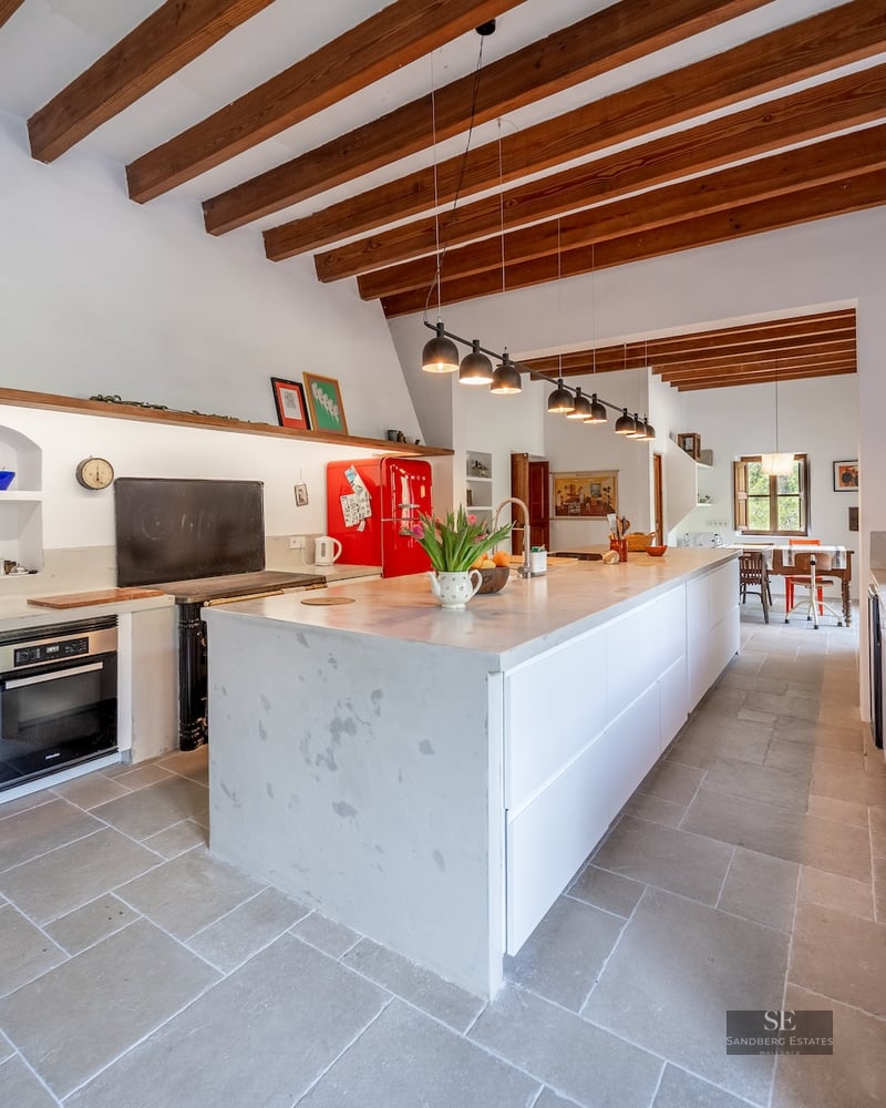 Spacious kitchen with exposed wood beams, a large white stone island, and a retro red refrigerator.