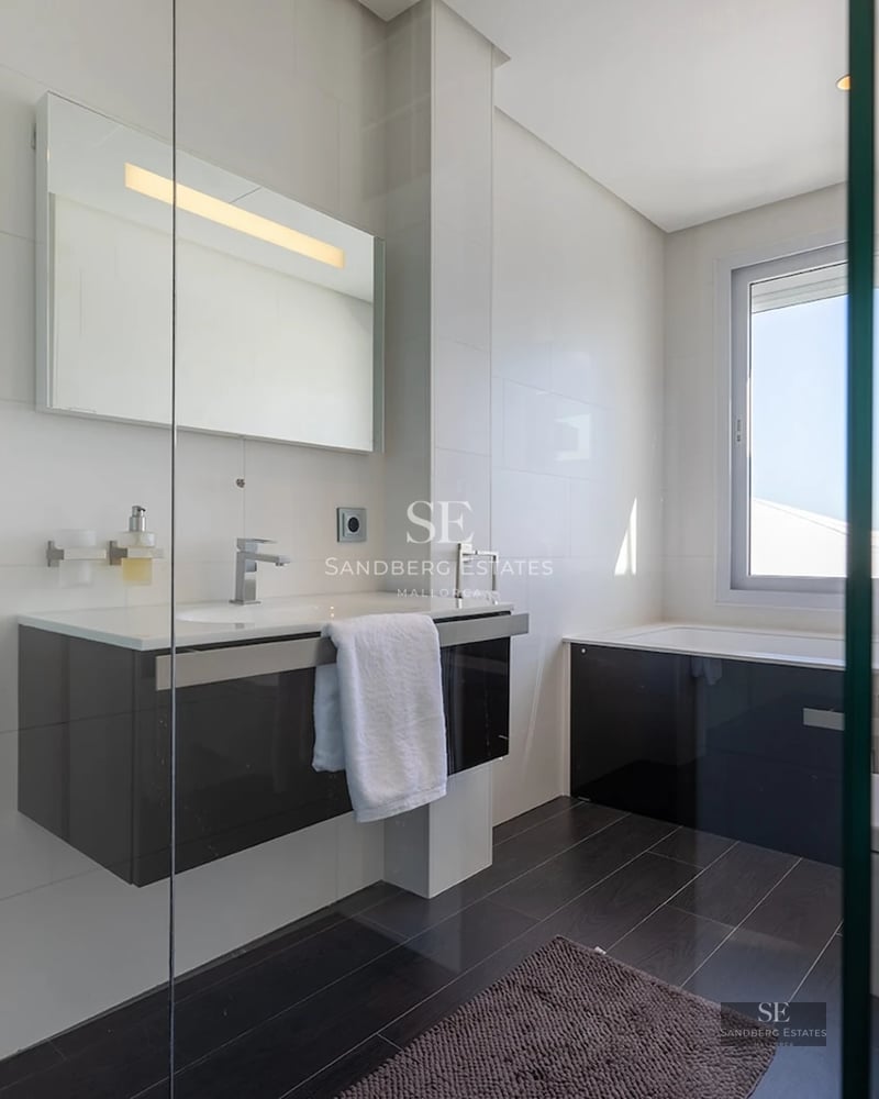 Bright modern bathroom featuring a floating dark vanity, illuminated mirror, glass partition, and a built-in bathtub.