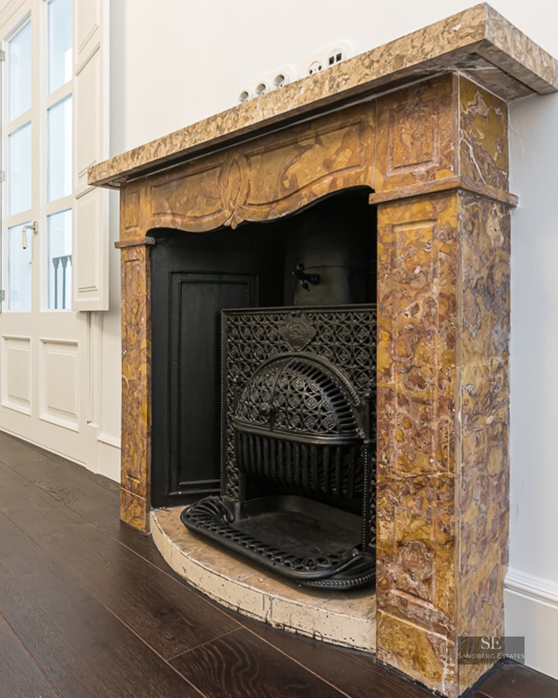 Ornate yellow marble fireplace with a decorative black cast iron grate on dark wood flooring against white walls.