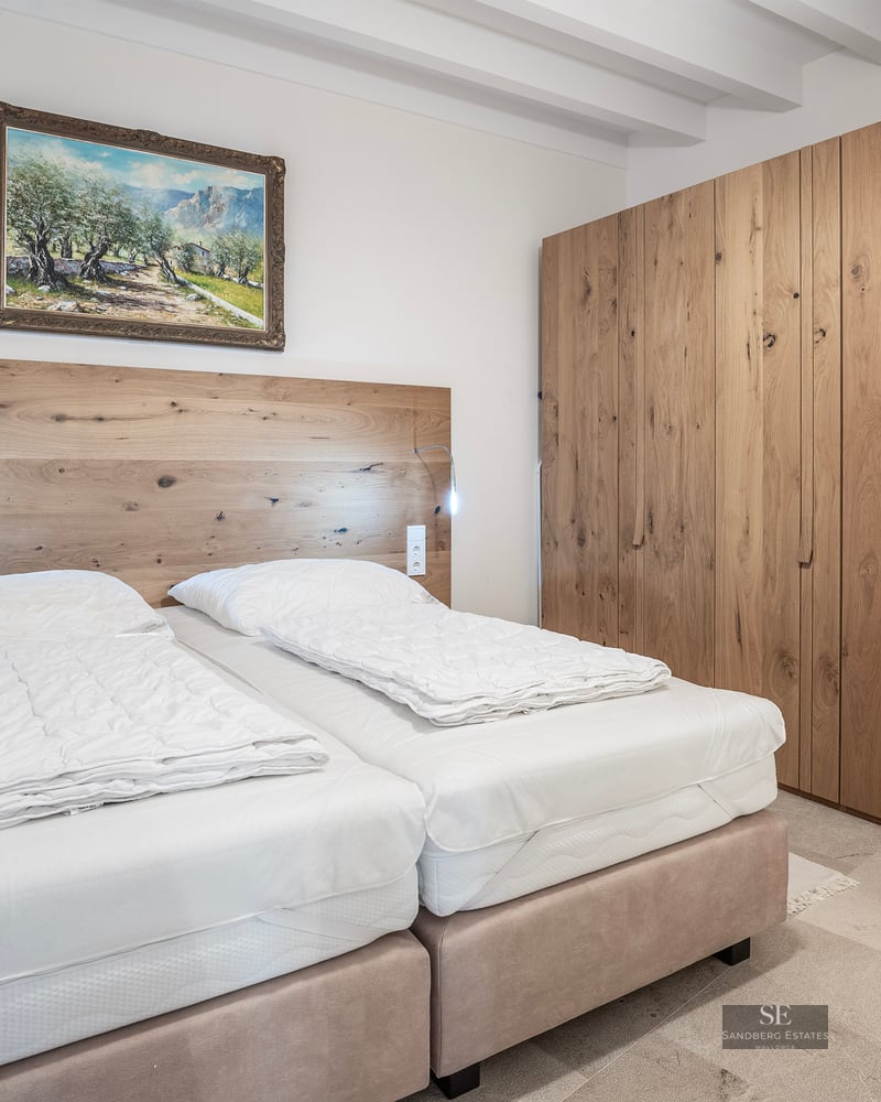 Bright bedroom with white beamed ceiling, large oak closet, and two beds with a wooden headboard.