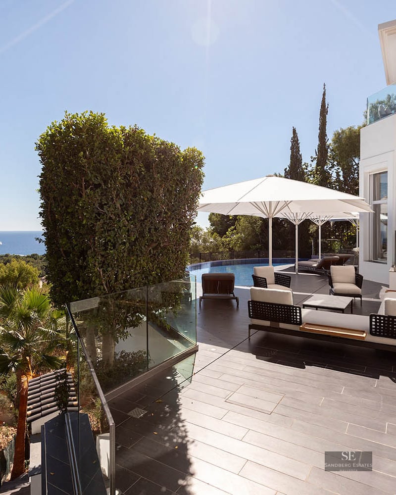 Modern terrace with designer lounge furniture, white umbrellas, and an infinity pool overlooking the sea.