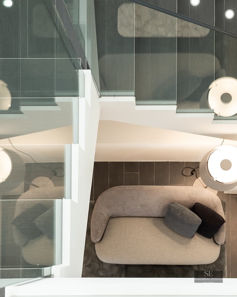 Overhead view of a staircase with glass railings looking down onto a grey sofa and a designer lamp.