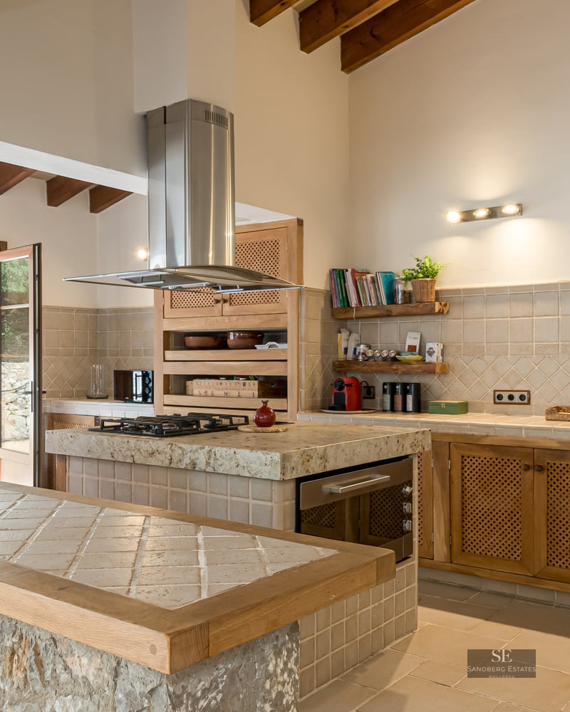 Spacious kitchen featuring exposed wood beams, a natural stone breakfast bar, and a tiled island with gas stove.