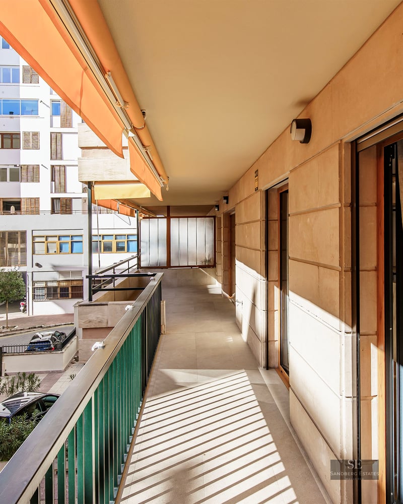 Long balcon ensoleillé avec auvent orange et balustrade métallique donnant sur une rue urbaine.