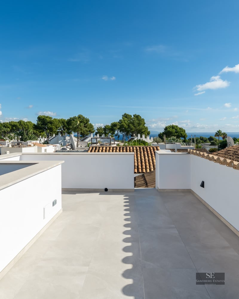 Spacious white rooftop with light stone tiling, offering panoramic views of palm trees, neighboring roofs, and the sea.