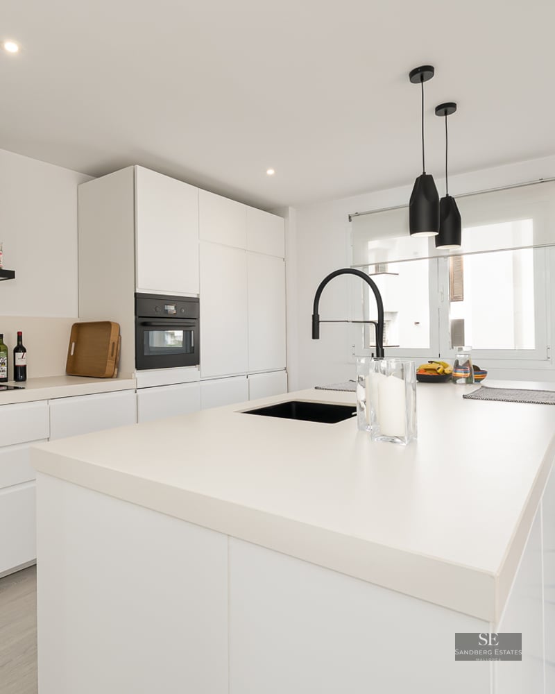 Modern white kitchen with a large island, black faucet, and sleek integrated appliances.