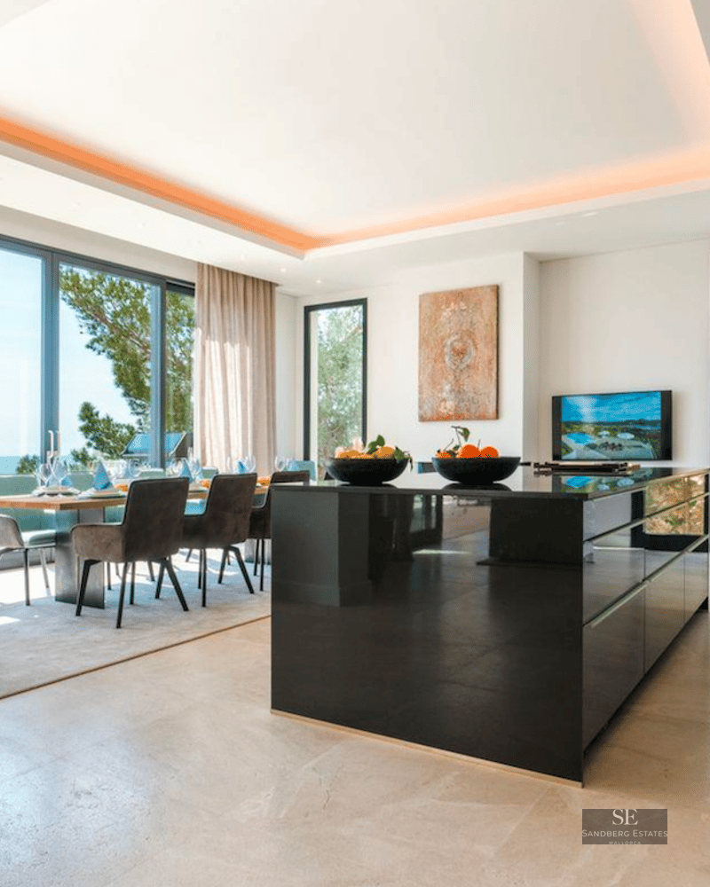 Modern kitchen and dining room with a black glossy island and large windows showing a bright sea view.