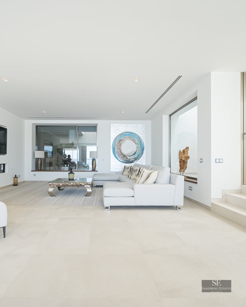 Bright minimalist living room with white sectional sofa, stone floors, linear fireplace, and modern art piece.