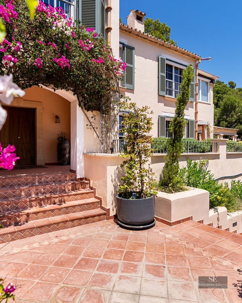 Terracotta steps leading to a wood door of a Mediterranean villa framed by pink bougainvillea.
