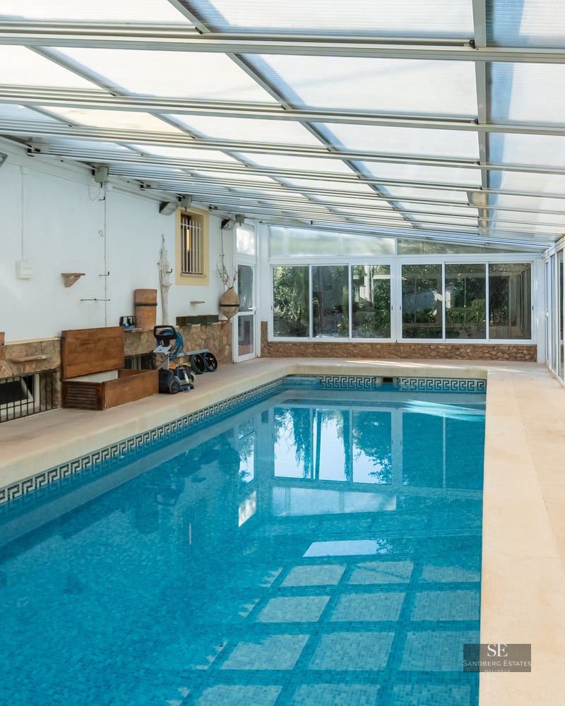 Indoor pool with blue mosaic tiles, stone accent wall, and translucent roof next to sliding glass doors.