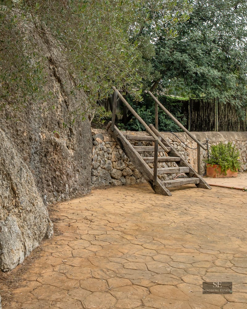Rustic outdoor patio featuring a natural stone cliff, wooden stairs, and lush green landscaping.