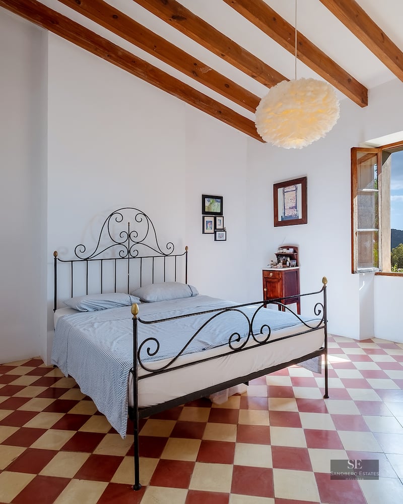 Bedroom with a black wrought iron bed, red and white checkered floor, exposed wooden beams, and a window with hill views.