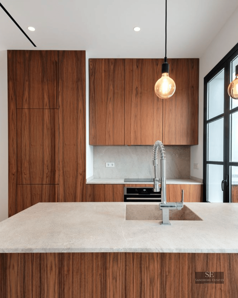 Modern kitchen featuring elegant walnut wood cabinetry, stone island with sink, and designer pendant lighting.