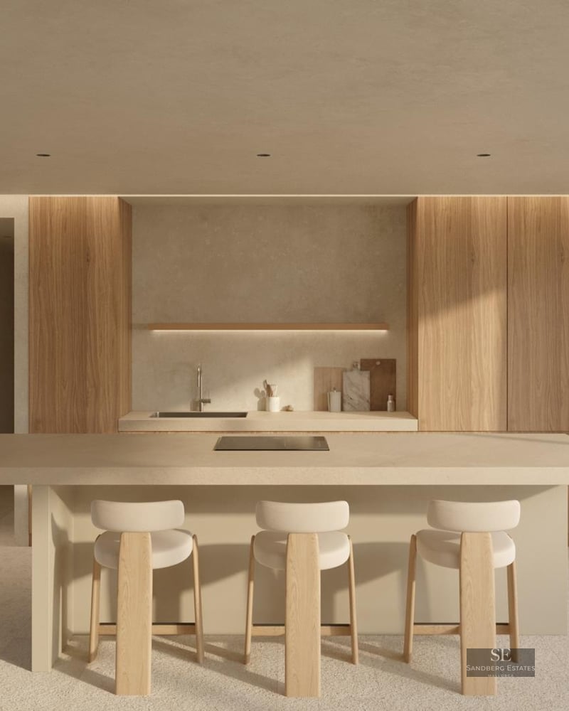 Modern minimalist kitchen featuring a large beige island, light wood cabinetry, and three stylish bar stools in a bright space.