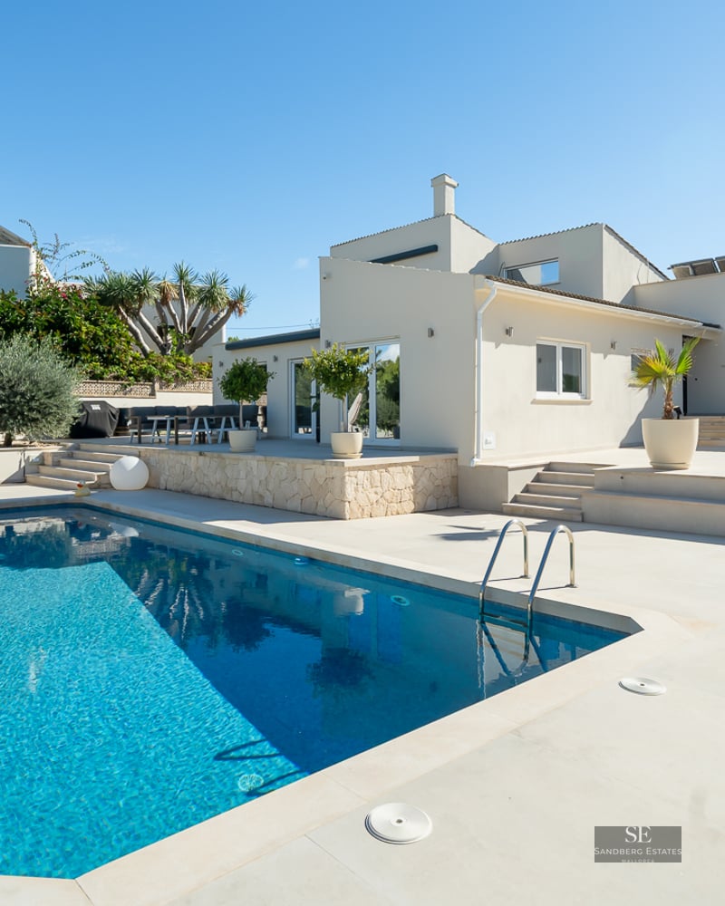 Piscine bleu éclatant à côté d'une villa blanche moderne avec une vaste terrasse en pierre sous un ciel dégagé.