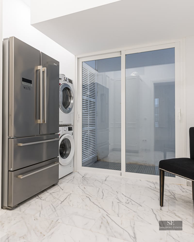 Utility room featuring a stainless steel refrigerator, stacked laundry unit, and white marble flooring.