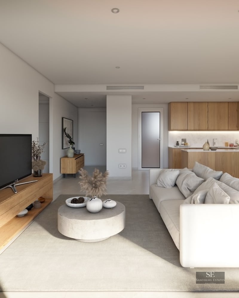 Bright modern living room with a white sofa, wooden furniture, and an integrated kitchen in the background.