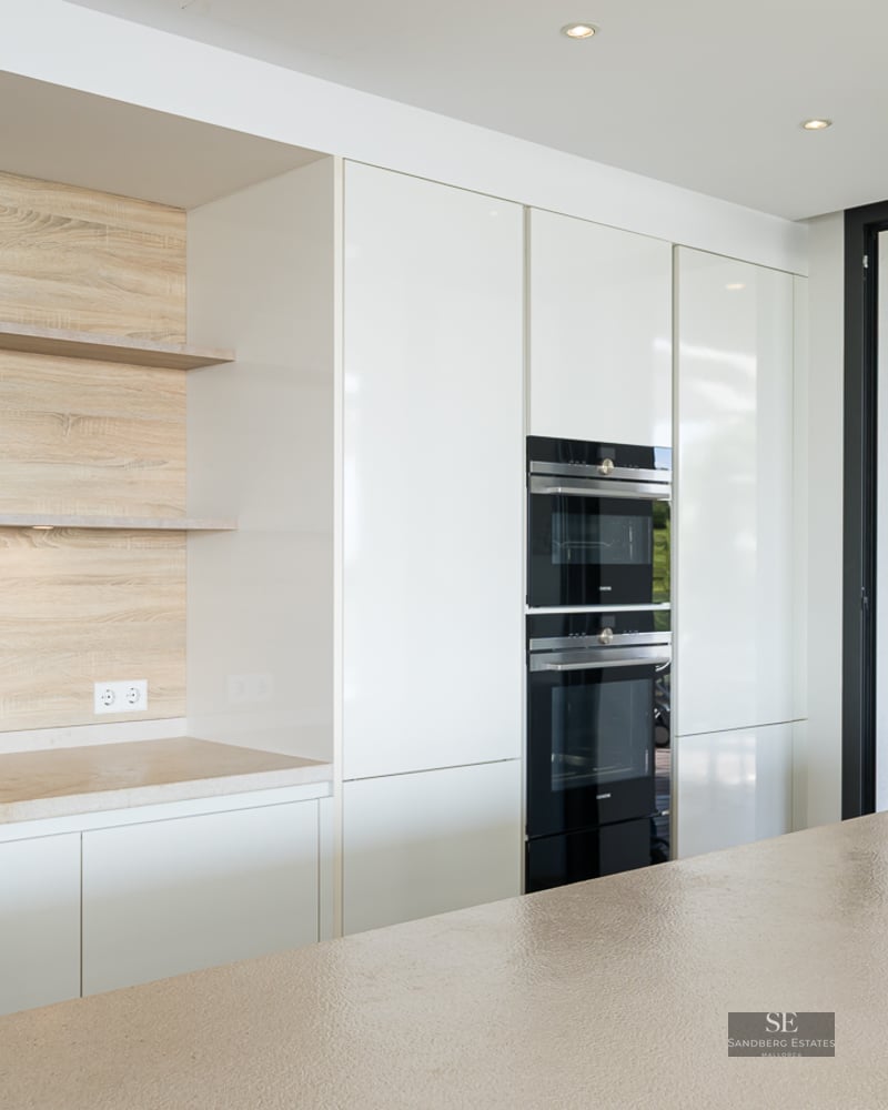 A modern kitchen featuring white cabinetry, wooden shelving, a stone island, and integrated high-end appliances.