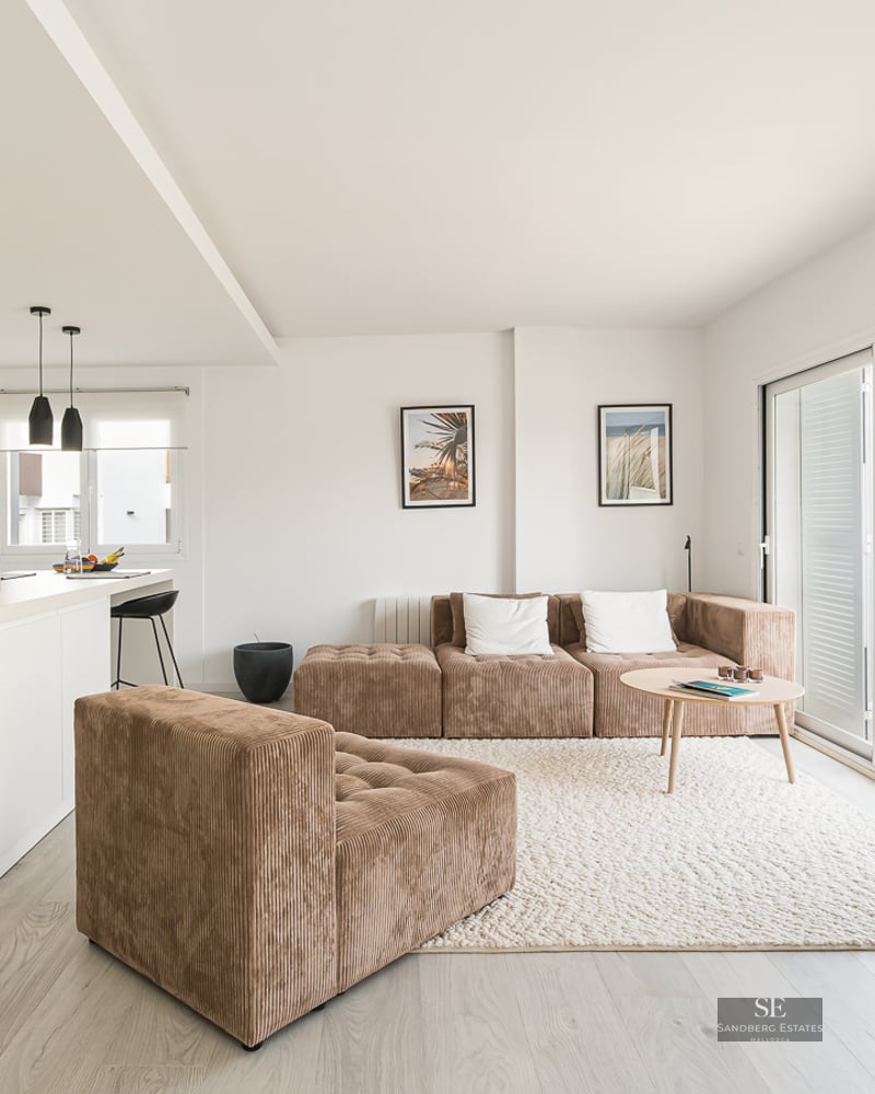 Bright modern living room with a brown corduroy modular sofa, textured rug, and a minimalist white kitchen.