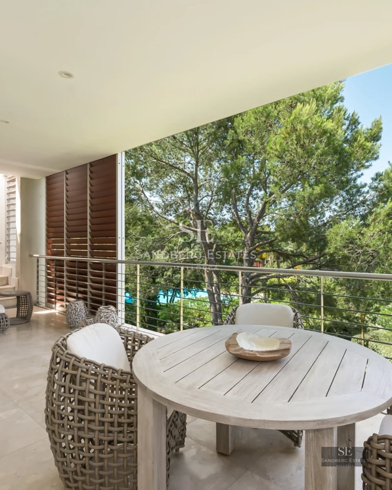 Aerial view of a luxurious villa with infinity pool, surrounded by greenery. Modern architecture with large terraces and windows.