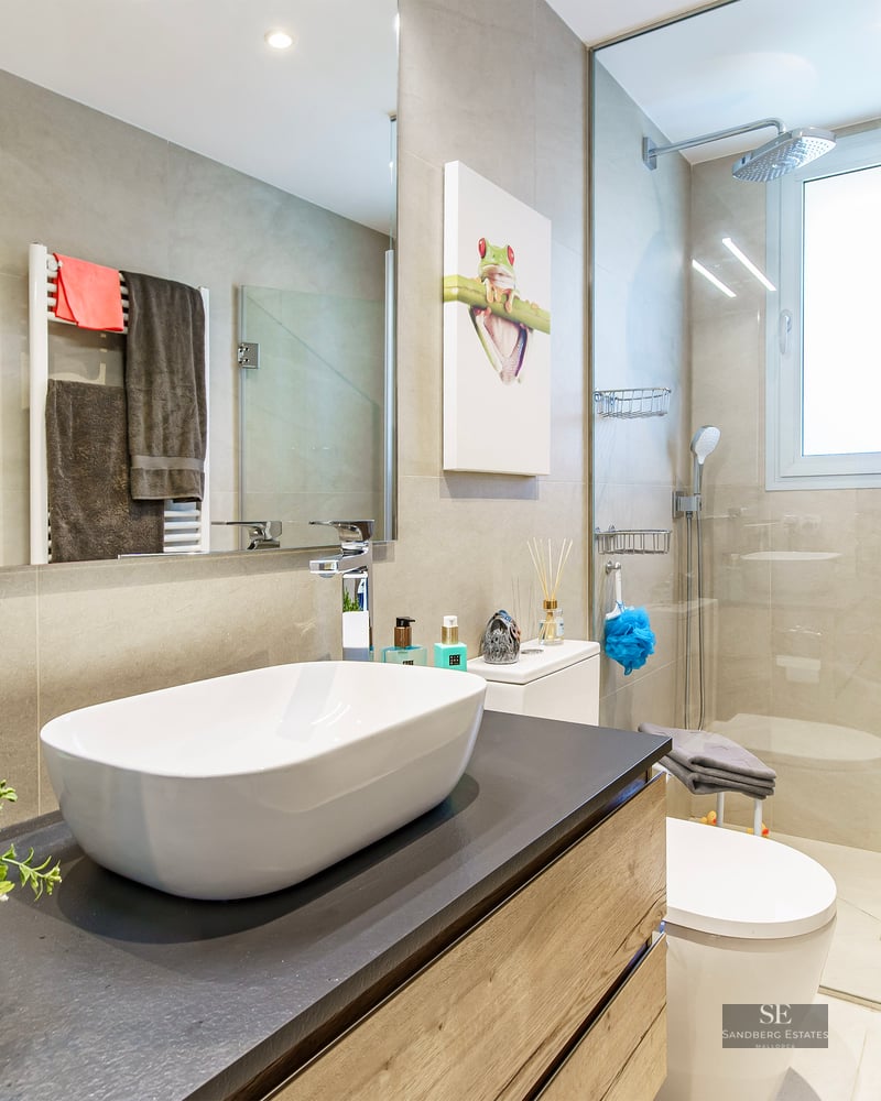 Modern bathroom featuring a white vessel sink on a dark vanity, glass-enclosed shower, and large mirror.