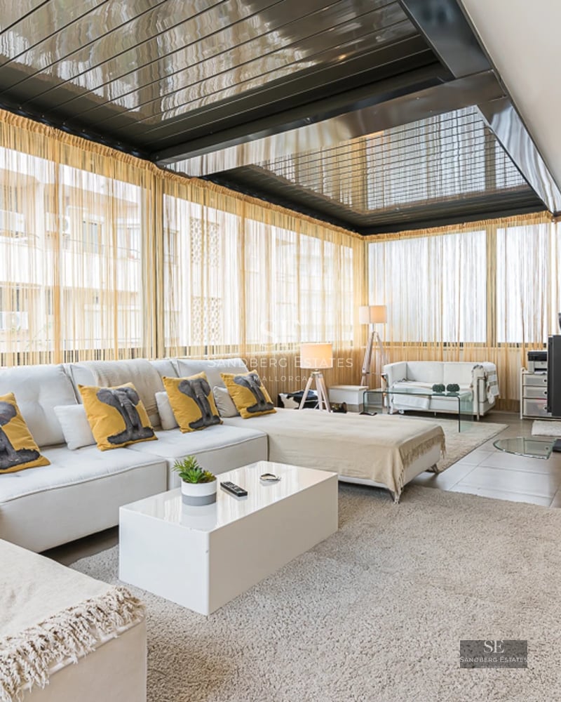 Spacious, bright living room with large windows, light wood floors, and minimalist decor. Beige sofa, coffee table, and access to terrace.