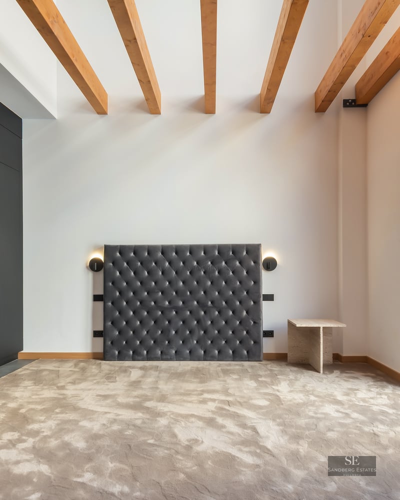 Bedroom featuring a grey velvet tufted headboard, wooden ceiling beams, black wardrobe, and large glass doors.