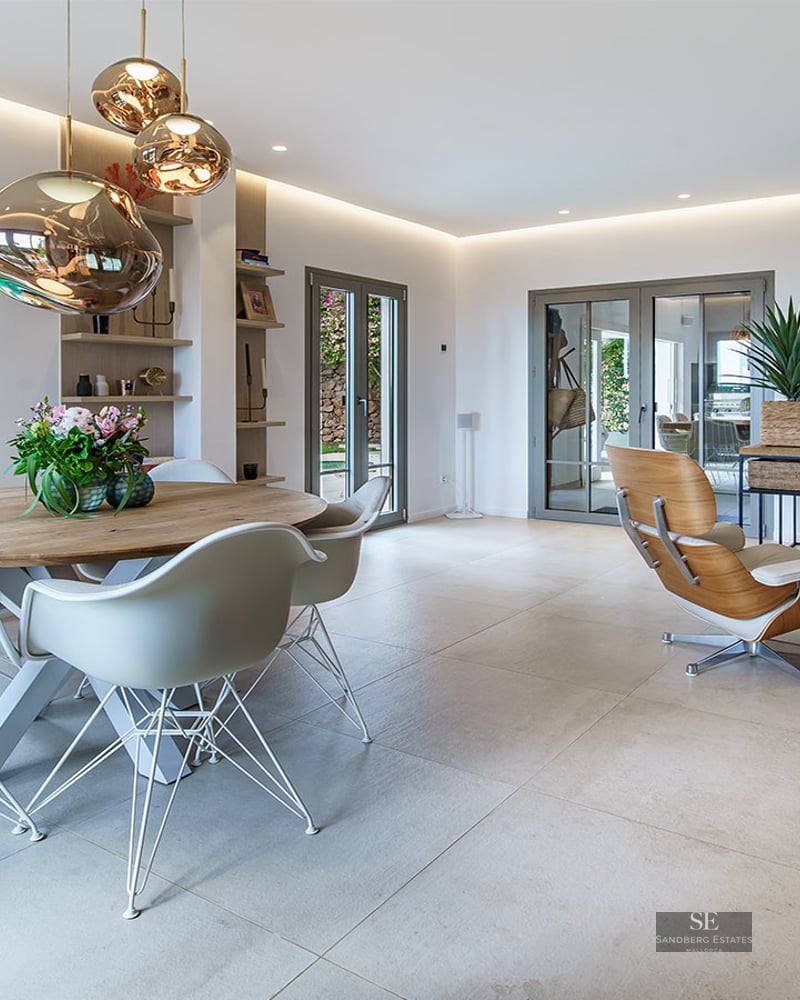 Modern open-plan living and dining room with designer furniture, tile floors, and glass doors to a green garden.