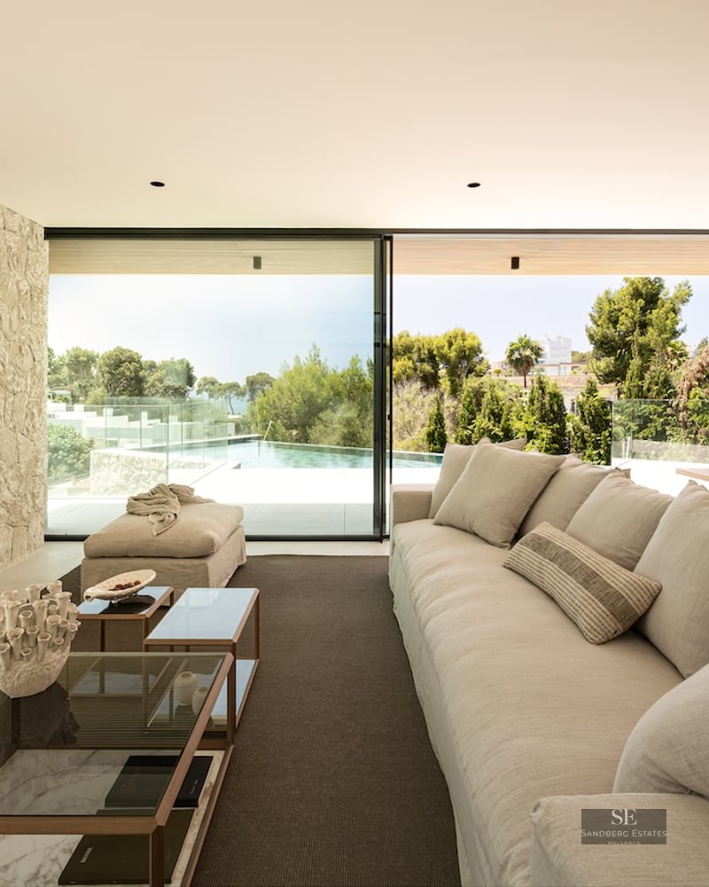 Living room with stone wall, beige sofa, and glass doors opening to a pool and garden view.