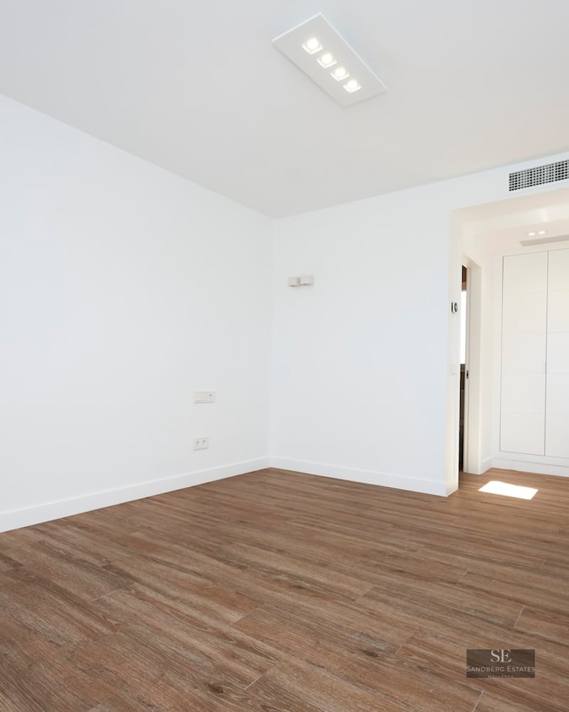 Empty modern room with white walls, wood-look flooring, and white built-in wardrobes in the background.