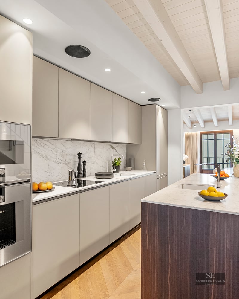 Modern kitchen with beige cabinets, white marble countertop, dark wood island, and light wood beamed ceiling.
