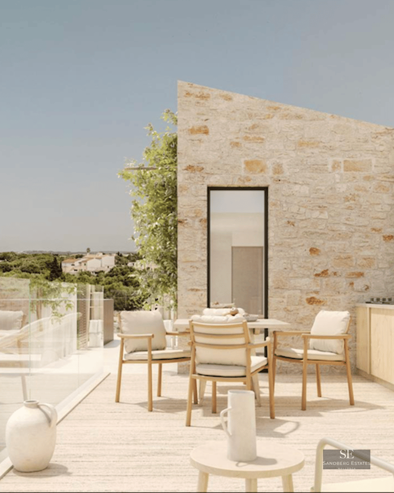 Modern stone terrace featuring a dining area, outdoor kitchen, and glass railing overlooking a scenic landscape.