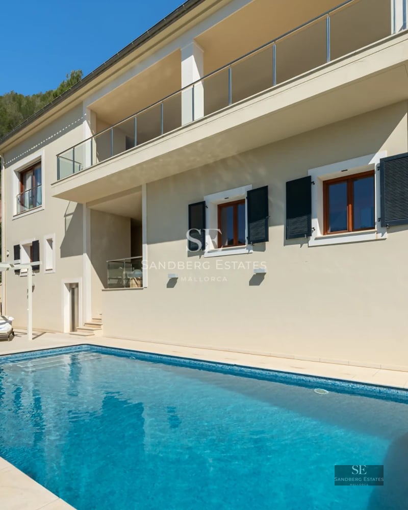 Exterior view of modern villa with pool, lush garden, and minimalist architecture. Large windows reflect the blue sky.