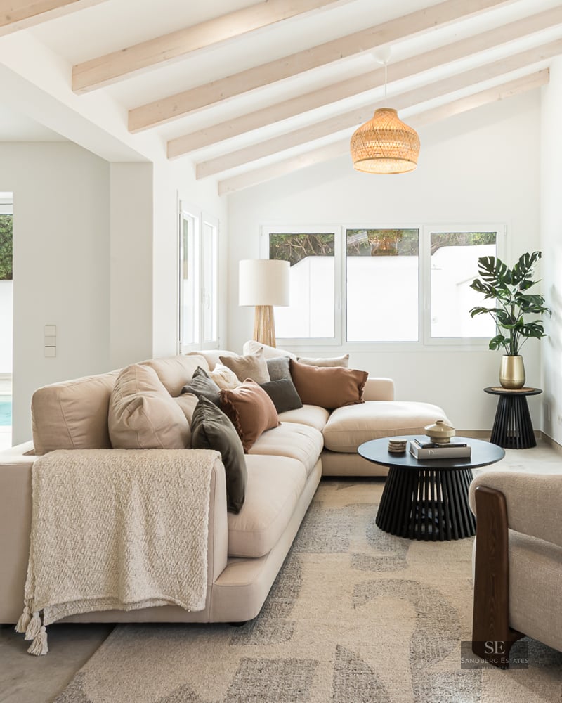 Bright living room with beige sectional sofa, wooden ceiling beams, and glass doors opening to a swimming pool.
