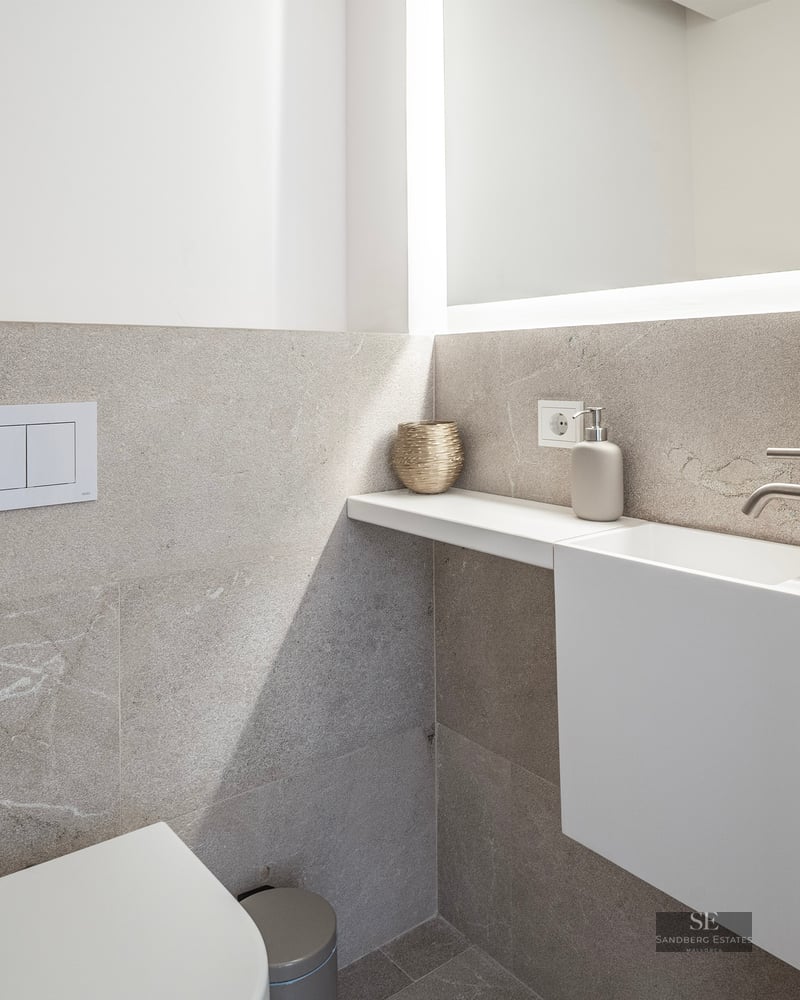 Modern powder room with textured stone tiles, a white floating sink, wall-mounted toilet, and a large backlit mirror.
