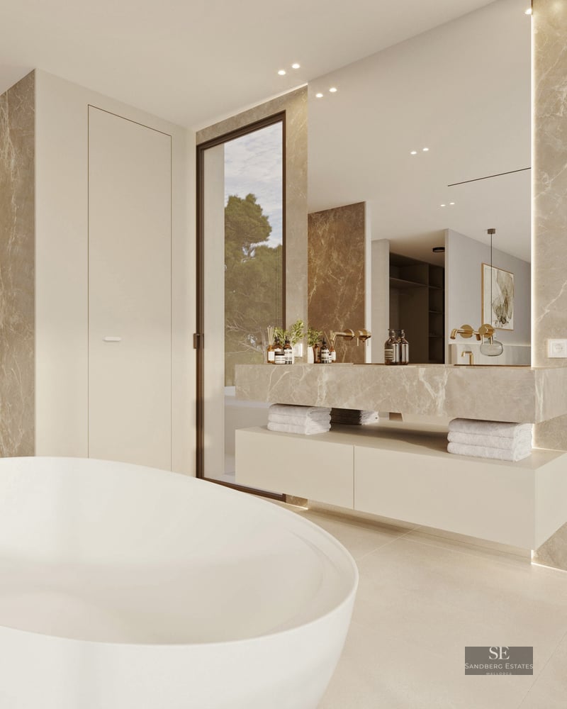 Modern master bathroom with white freestanding tub, beige marble walls, and elegant gold fixtures.