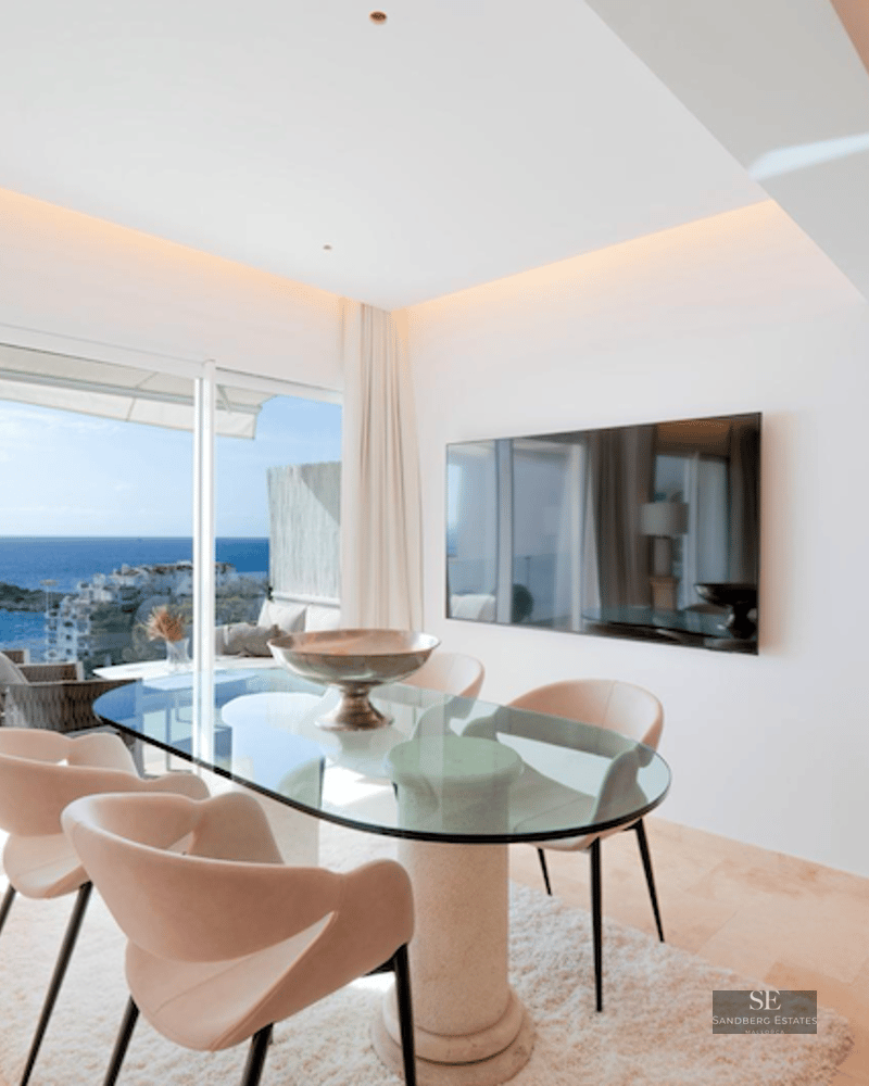 A modern dining room with a glass table, designer chairs, and large windows overlooking the Mediterranean sea.