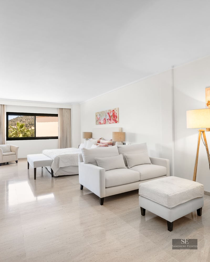 Suite lumineuse avec canapé blanc, armoires en bois, grand lit et art floral sur sol en marbre poli.