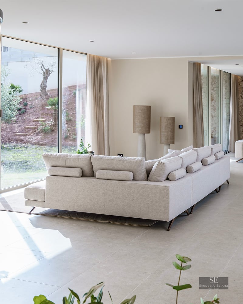 Spacious modern living room with cream sectional sofa, large glass walls viewing a garden, and stone accent wall.