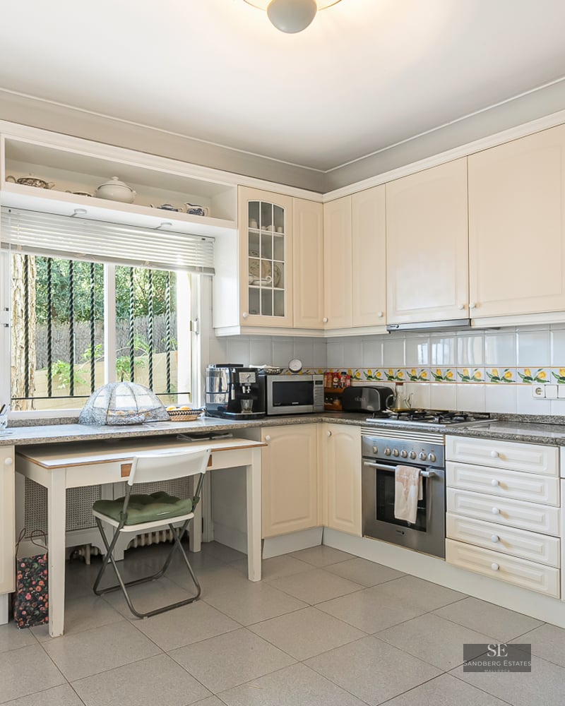 Spacious cream kitchen with granite counters, small dining table by a window, and integrated appliances.