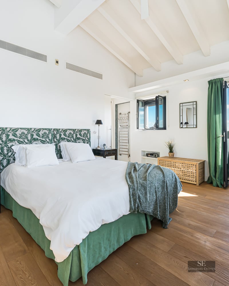 Bright master bedroom with high ceilings, white beams, and a balcony overlooking the Palma Cathedral.
