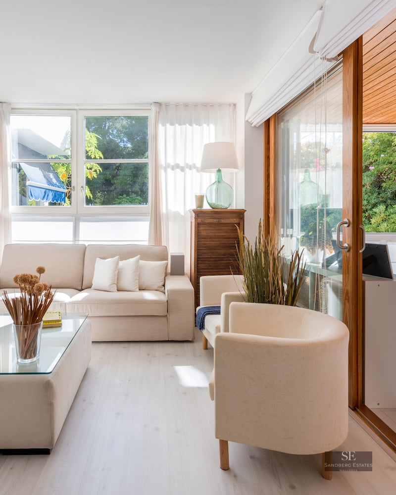 Bright living room with cream sofas and large sliding glass doors leading to a wooden terrace area.