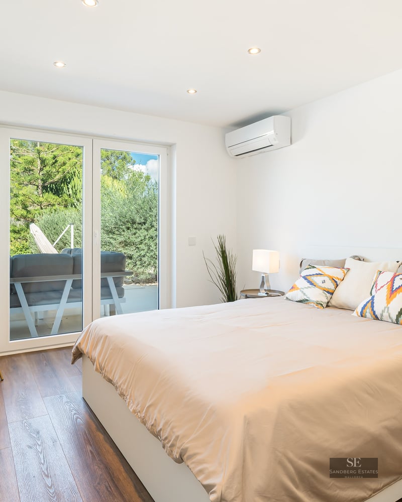 Chambre lumineuse avec grand lit, parquet en bois et portes vitrées coulissantes donnant sur un jardin.