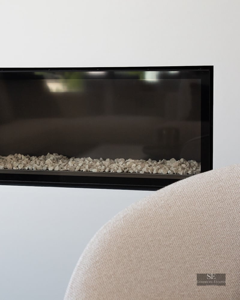 Close-up of a rectangular black-framed fireplace built into a white wall with white stones inside.