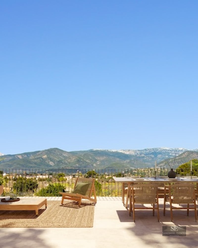 Spacious sun-drenched terrace with wooden furniture, dining area, and stunning views of distant mountains.