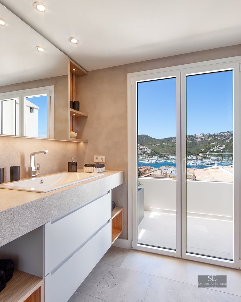 Modern bathroom with stone vanity, large mirror, and glass doors opening to a balcony with a marina view.
