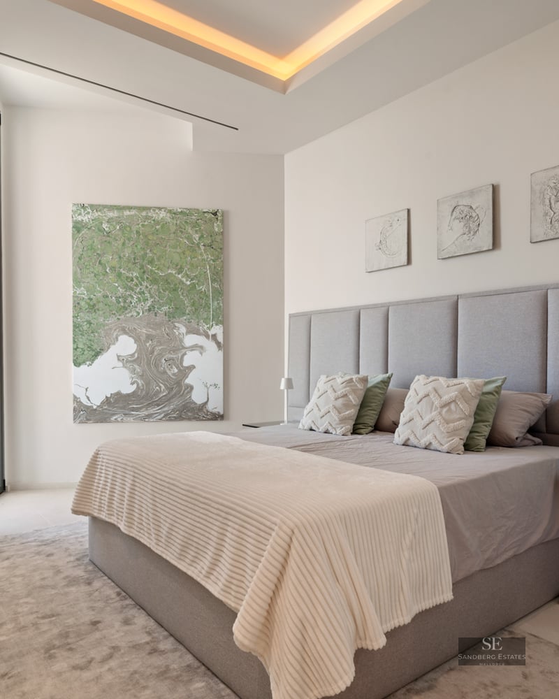 Bedroom with grey upholstered headboard, king-size bed, abstract art, and warm recessed lighting.
