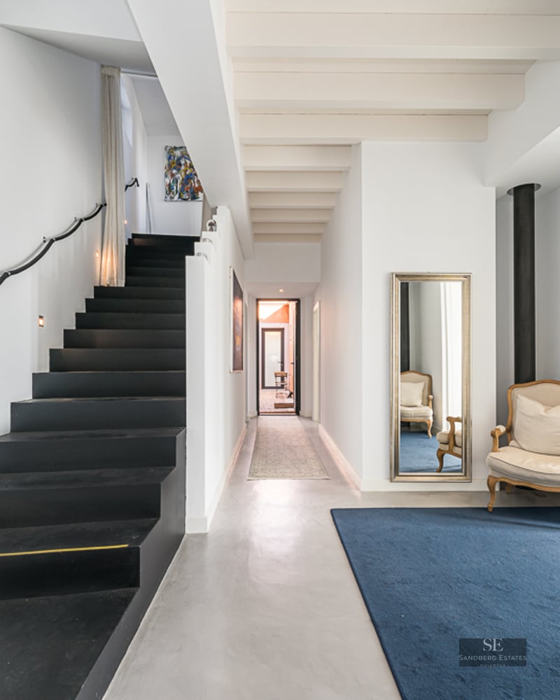 Modern entryway featuring a sleek black staircase, polished concrete floors, and a blue rug with a classic armchair.