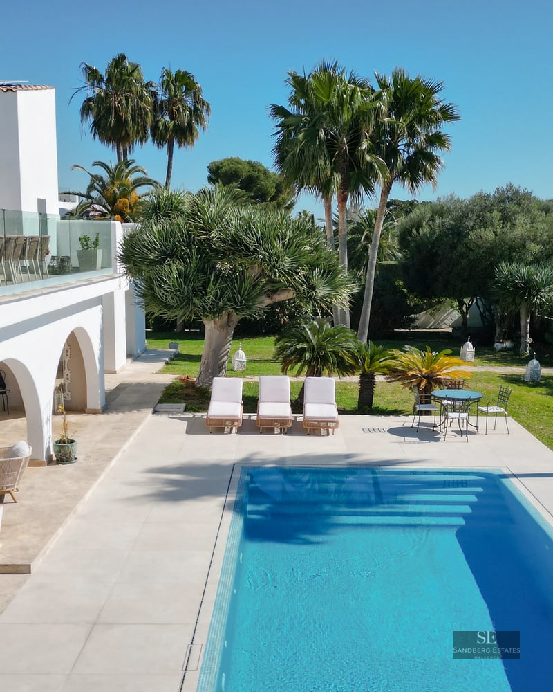 Modern white villa with rectangular blue pool, tropical garden, and glass-railed upper terrace.